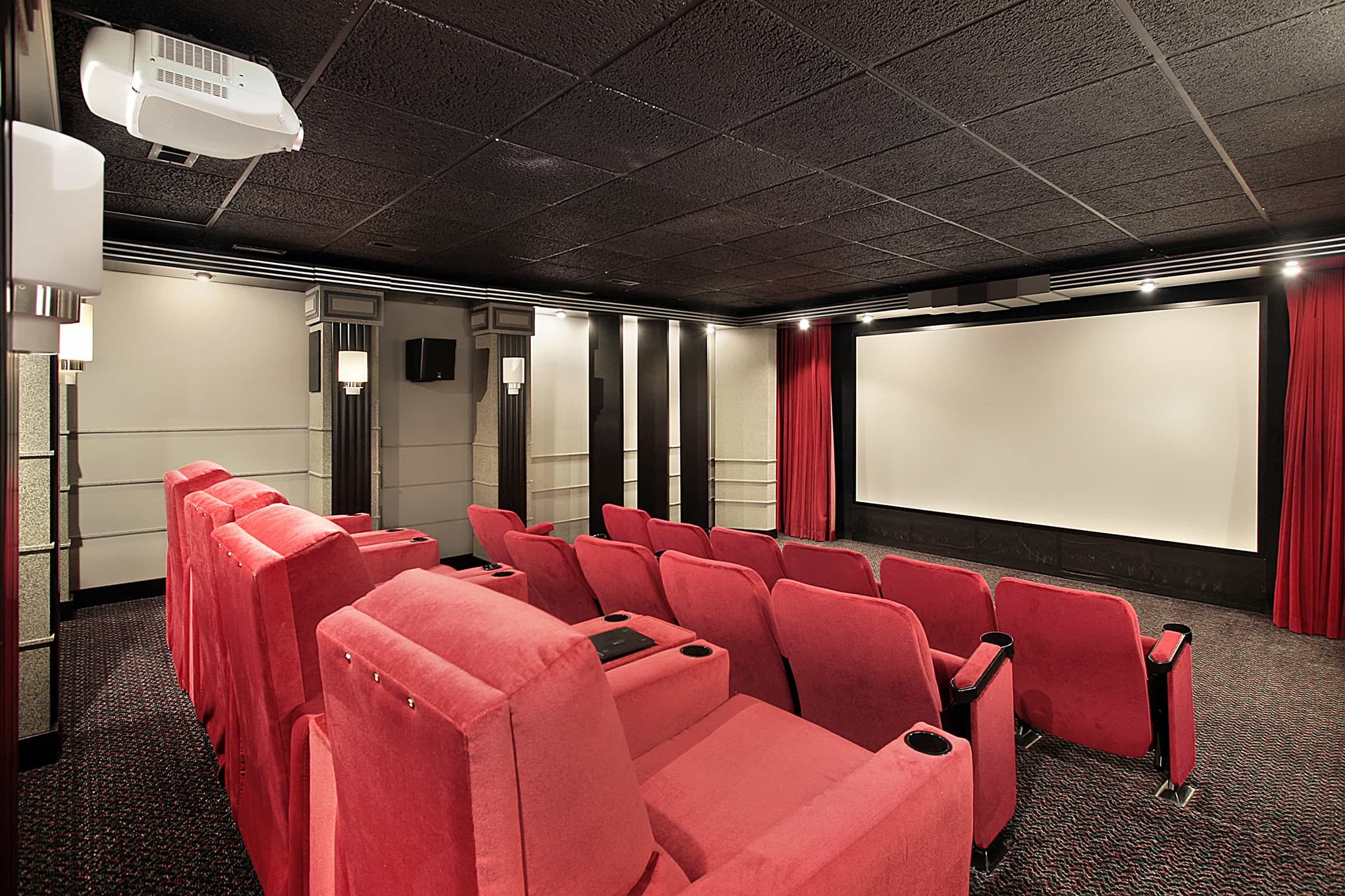 red black and white color themed at home theater with red seats, red wall, and large screen on wall.